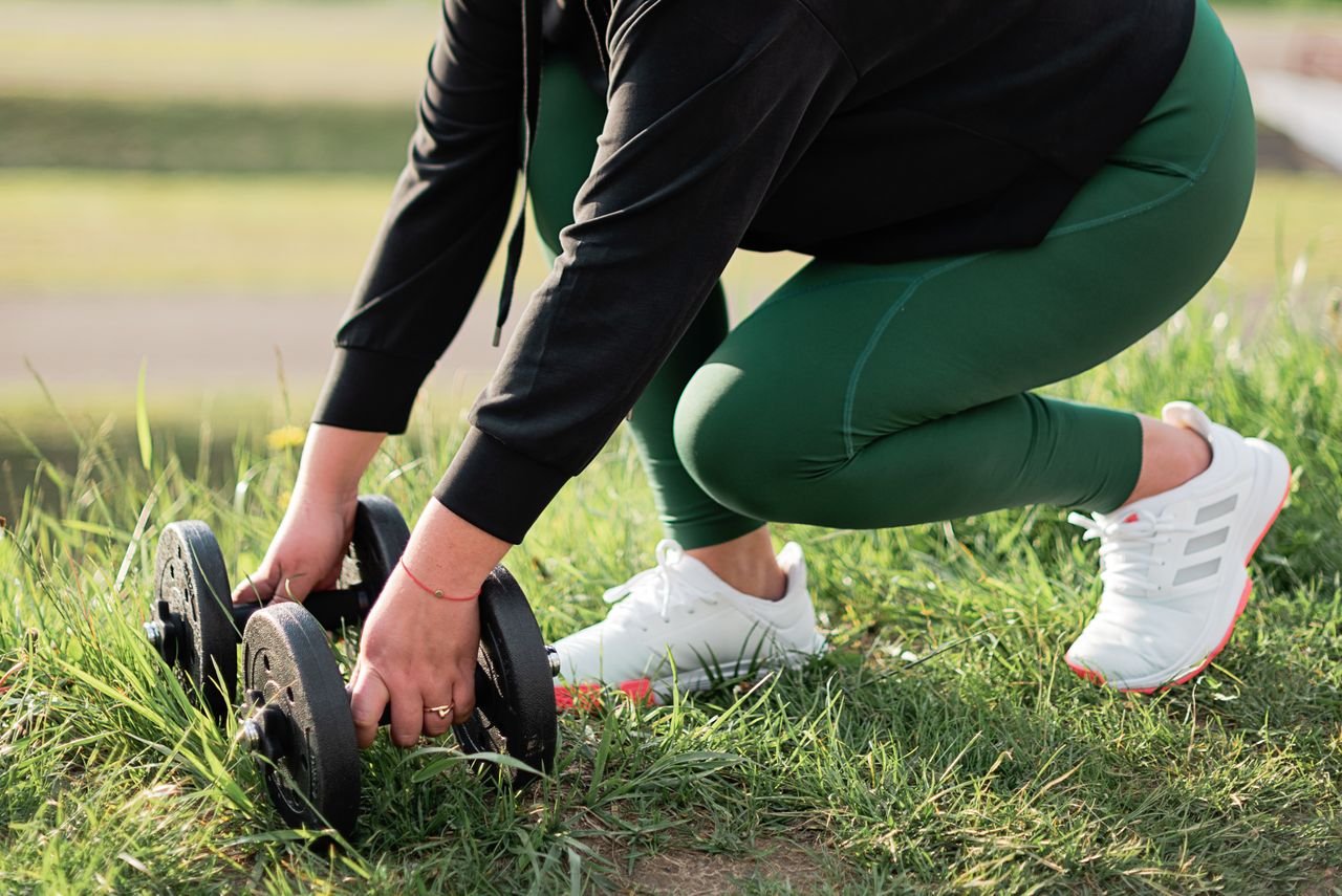 Close-up of a woman picking up dumbbells in a park setting, emphasizing outdoor workout routines.